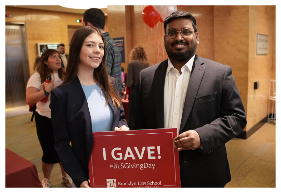 a woman and a man take a photo while holding either side of a sign that reads "I Gave! #BLSGivingDay"